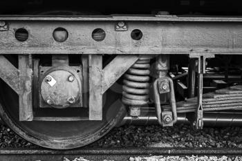 Old rusted railway carriage wheel with suspension details, stylized black and white photo