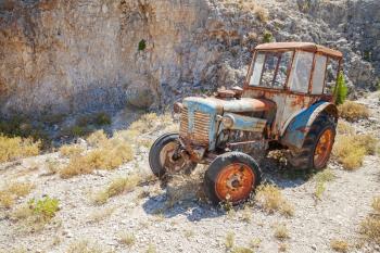 Old abandoned rusted tractor stands on dry summer meadow in Greece