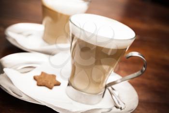 Glass mugs full of Cappuccino coffee stand on wooden table in cafeteria. Closeup photo with soft selective focus
