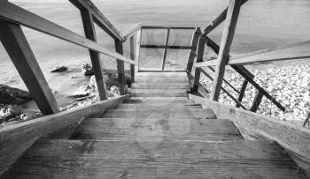Perspective view of wooden stairs going down to the sea coast. Black and white photo