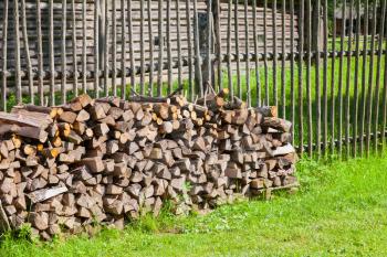 Firewood stacked on summer green grass near old wooden rural fence