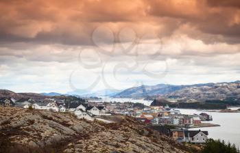 Coastal Norwegian landscape. Fishing village with colorful houses under colorful dramatic cloudy sky. Rorvik, Norway