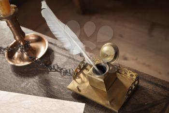 Old writing materials on wooden table. Brass inkwell, white pen and old paper