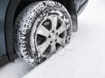 Modern car wheel with studded tire stands on winter road with deep snow, close-up photo with selective focus