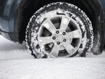 Modern car wheel with studded tire stands on winter road with deep snow, close up photo with selective focus