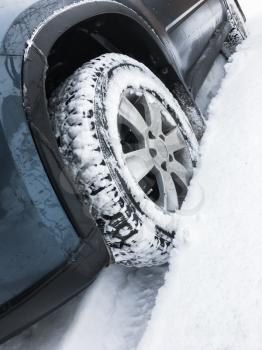 Modern blue car fragment, wheel with studded tire standing on winter road with deep snow, close-up photo with selective focus