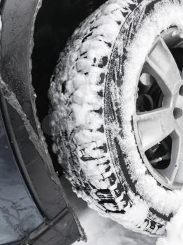Car wheel with studded tire standing on winter road with deep snow, closeup photo with selective focus