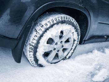 Modern car wheel with studded tire standing on winter road with deep snow, blue toned photo with selective focus