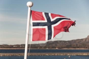 Norwegian national flag over blue sky background, vintage toned photo
