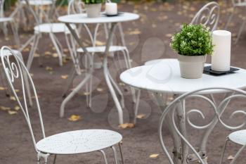 Outdoor restaurant background interior, metal white chairs and tables with decorative green plants in pots and candles 
