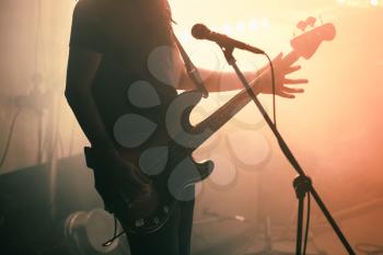 Silhouette of bass guitar player on the stage with bright warm illumination, live music theme
