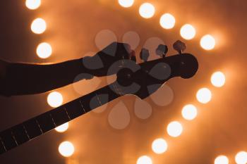 Live music background, guitarist tunes electric bass guitar, close-up silhuette photo with soft selective focus
