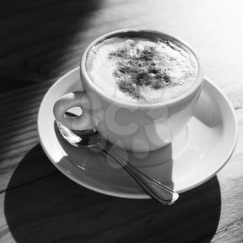 Cappuccino. Cup of coffee with milk foam and cinnamon powder stands on wooden table, square black and white photo