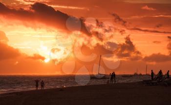 Caribbean seascape at sunrise. Atlantic ocean coast, ordinary people walking on sandy beach in red morning sunlight
