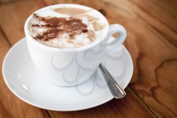 Cappuccino. Cup of coffee with milk foam and cinnamon powder stands on wooden table