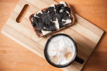 Cup of cappuccino and sandwich with black caviar stand on wooden table, top view, closeup photo with selective focus