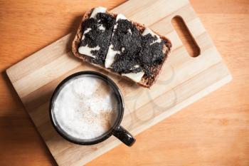 Cup of cappuccino and a sandwich with black caviar stand on wooden table, top view, selective focus