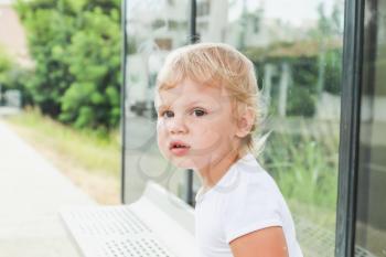 Close-up portrait. Cute Caucasian blond baby girl waits on a bus stop