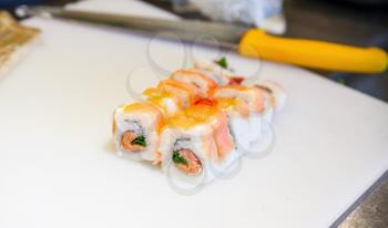 Traditional Japanese sushi rolls with salmon lay on white cutting board with chief knife. Closeup photo with selective focus
