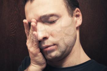 Young stressed Caucasian man with closed eyes. Studio portrait over dark wall background