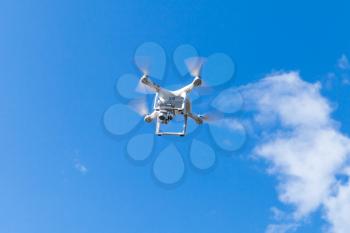 White quadrocopter in blue cloudy sky, compact drone controlled by wireless remote