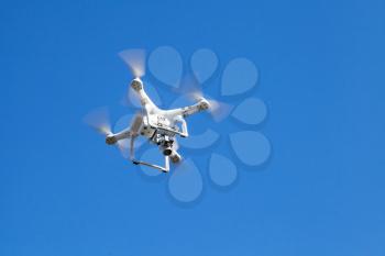 White quadrocopter in blue sky, compact drone controlled by wireless remote