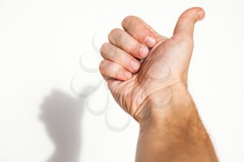 Male hand shows thumbs up gesture over white wall background with soft shadow, like it concept
