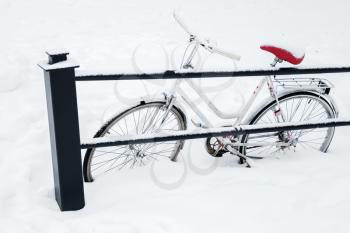 White bicycle parked near urban railings in snowdrift. European winter