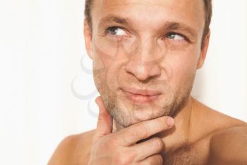Close up face portrait of young adult shirtless thinking Caucasian man over white wall background