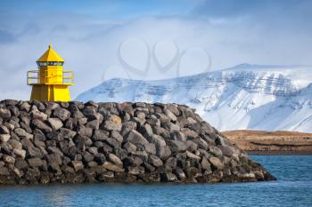 Yellow lighthouse tower on stone breakwater, entrance to Reykjavik port