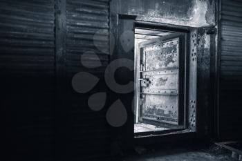 Abstract dark grungy industrial interior with metal walls and open heavy steel door, blue toned monochrome photo