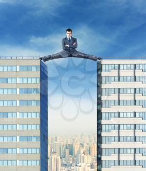 Businessman sits in the splits between two high buildings against the city
