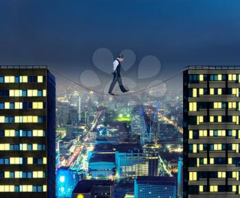 Businessman thinking going the tightrope between two buildings at night