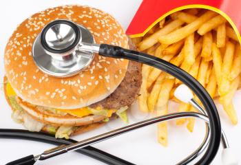 Fried potatoes and burger with medical stethoscope
