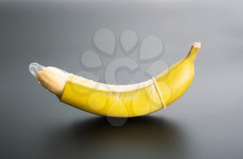Banana with condom on grey background