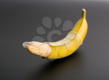 Big banana with condom on grey background