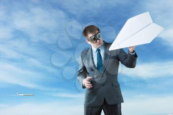 Businessman with paper plane and wearing goggles isolated on sky background