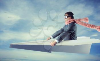 Businessman flying on big paper plane and wearing goggles and scarf isolated on sky background