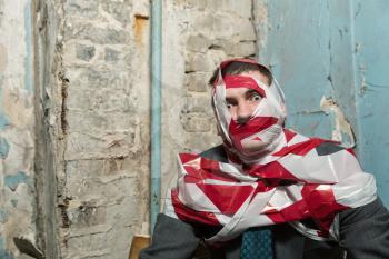 Victum man with stripped  red and white duct tape over body in old house