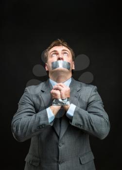 Man with mouth and hands covered by masking tape preventing speech, isolated on black