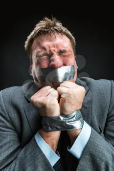 Man with mouth and hands  covered by masking tape preventing speech, studio shoot