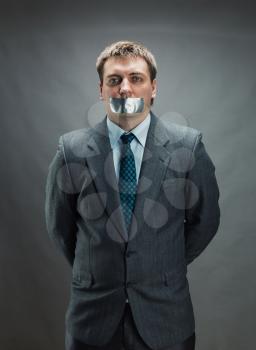 Man with mouth and hands covered by masking tape preventing speech, isolated on gray