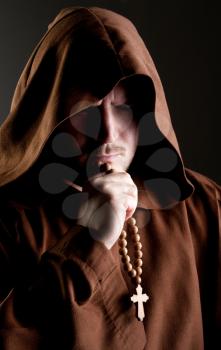Portrait of medieval monk with cross rosary in shadow
