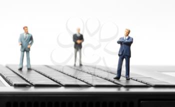 Miniature figurines of successful businessman and team standing on laptop keyboard