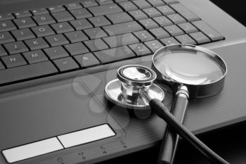 Medical stethoscope and magnifying glass on laptop keyboard. In B/W