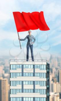 Woman holding a red flag stands on the top of a high building