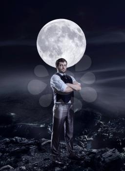 Businessman standing with crossed arms in the night agaist big moon