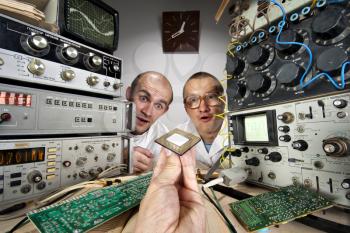 Two funny nerd scientists at vintage technological laboratory looking at modern computer processor
