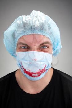 Mad mental sick surgeon with blood smile on mask