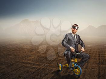 Odd businessman riding a small bicycle against desert background